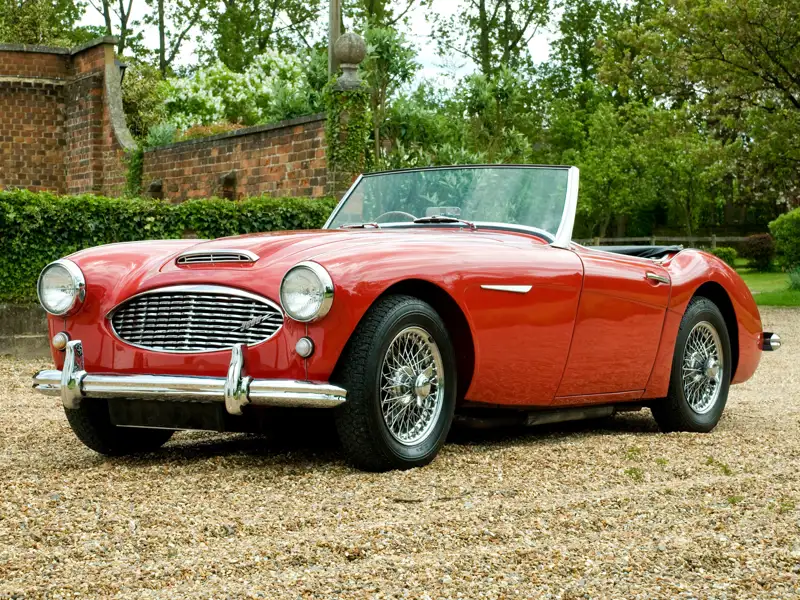 A classic red convertible sports car parked in a grassy area.
