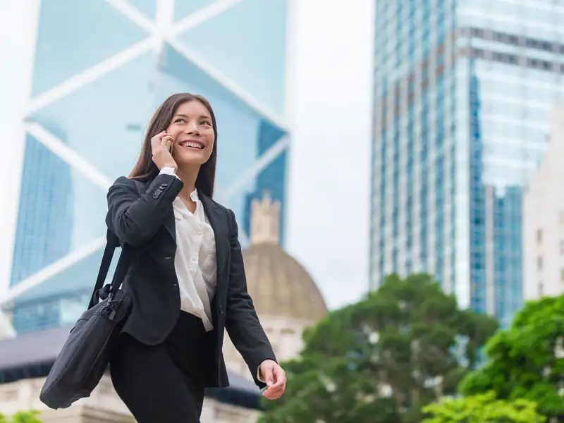 A professional walks in a sunny downtown area, speaking on a mobile device.