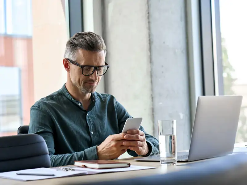 A mature man with glasses smiles as he looks at information on a mobile device.