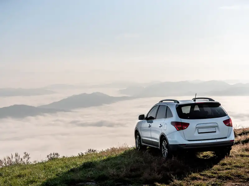 A sport utility vehicle parked on a hilltop, overlooking a cloud-filled valley.